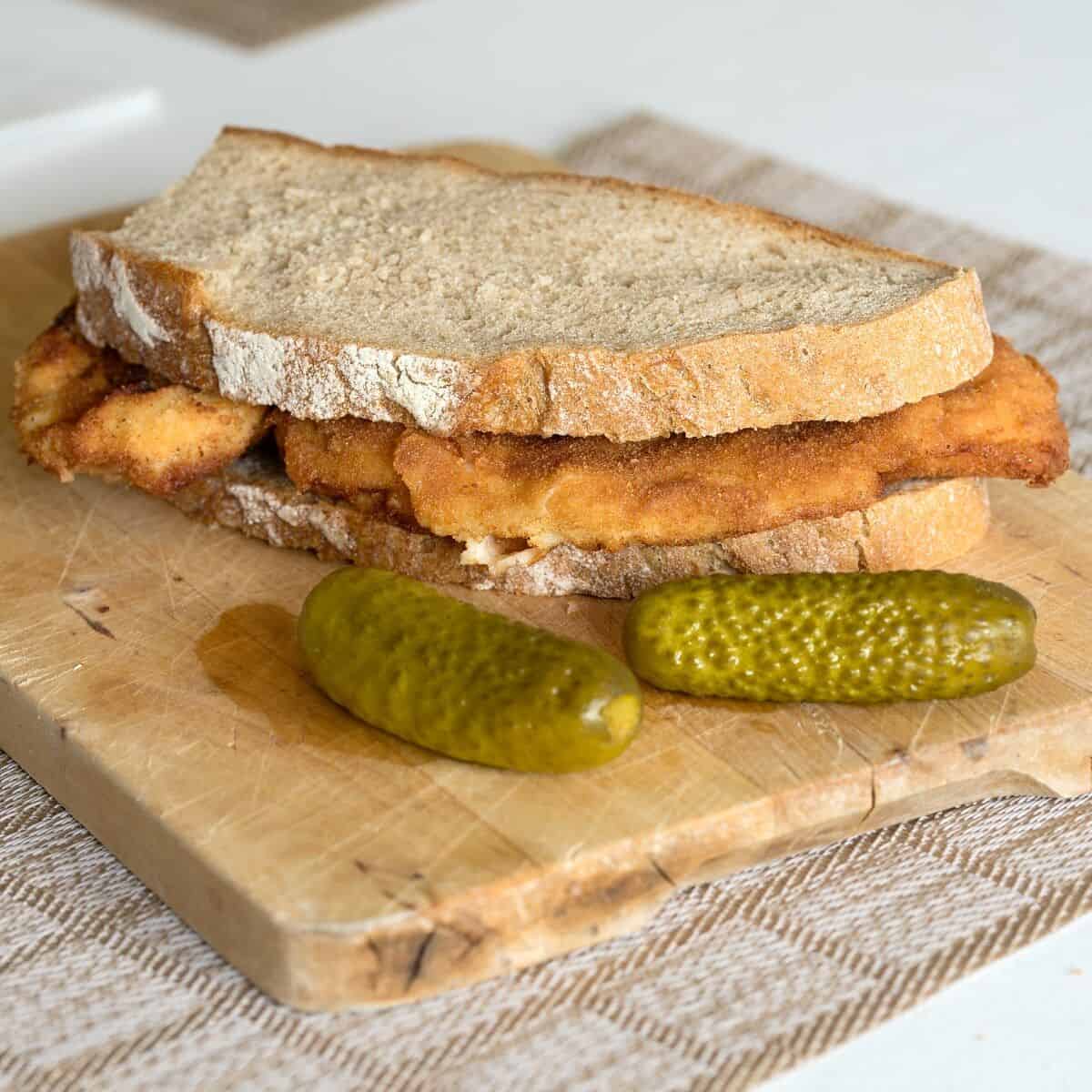 Czech řízek tucked between two slices of bread, with dill pickles.
