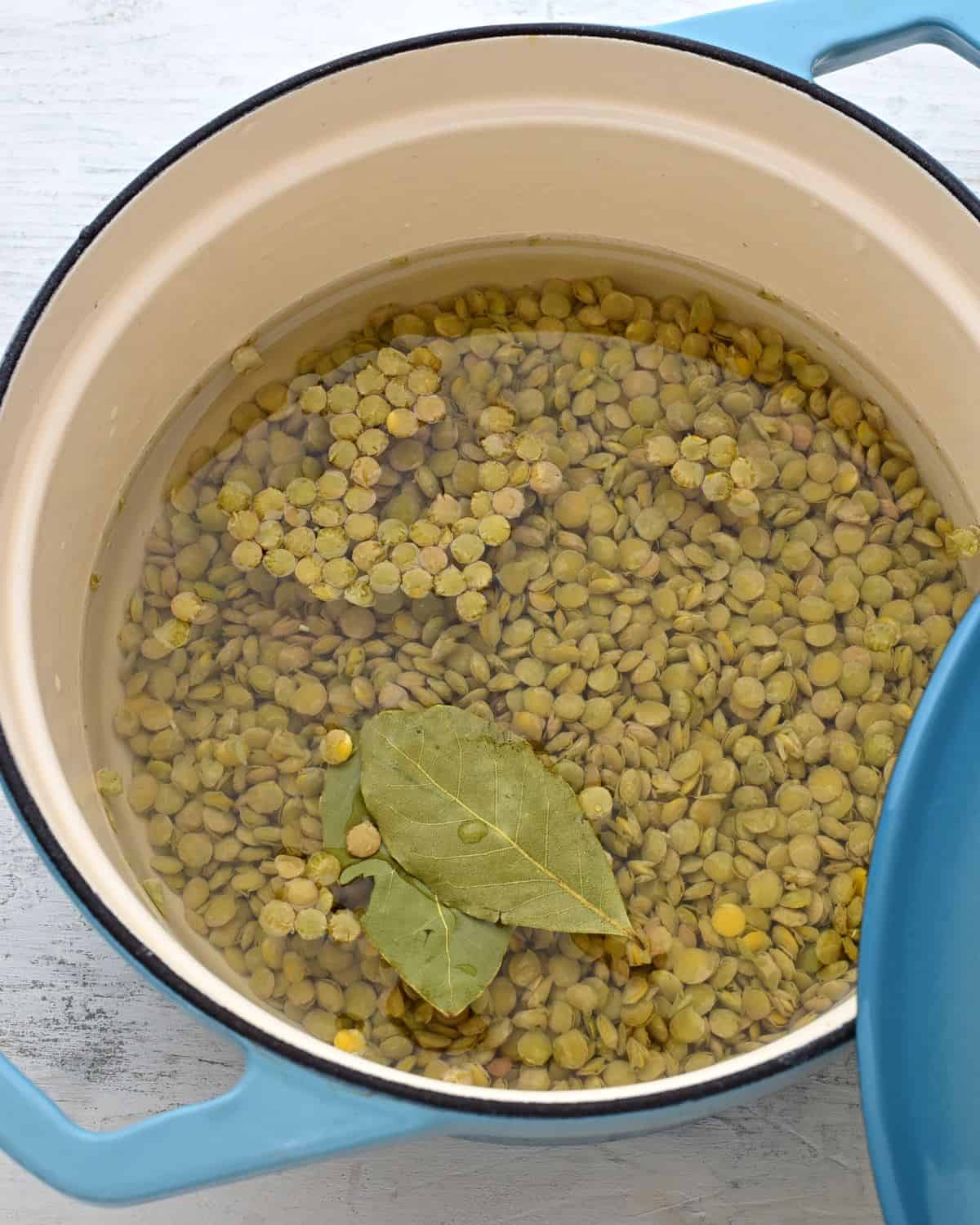 Lentils in a pot with bay leaves, covered with water.
