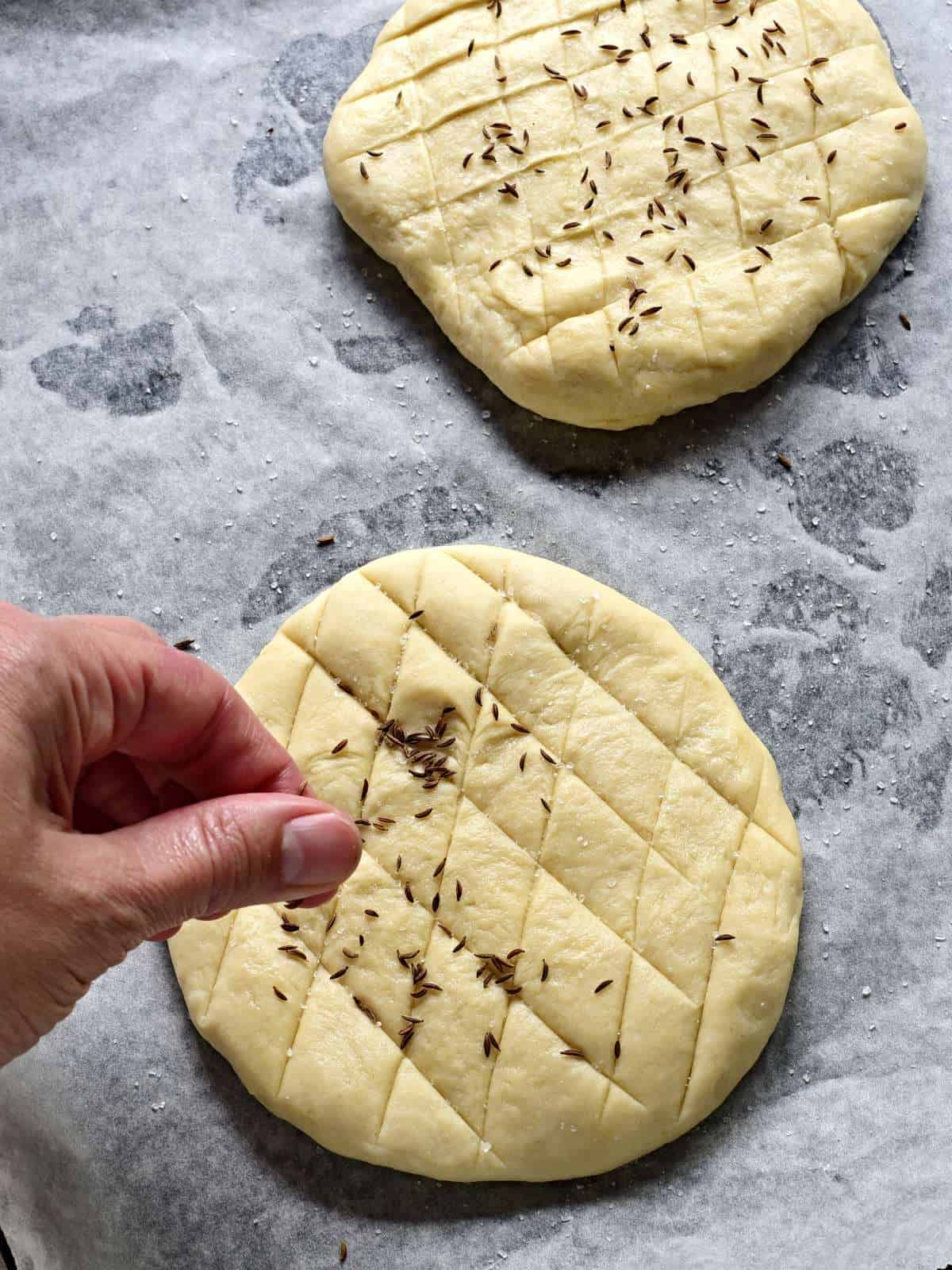 Sprinkling flatbread with salt and caraway seed before baking.