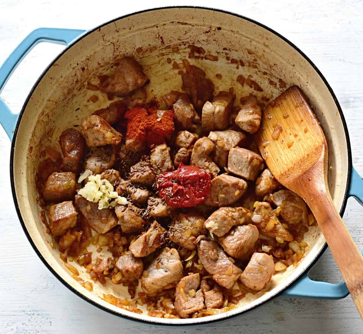 Adding spices to pork goulash.