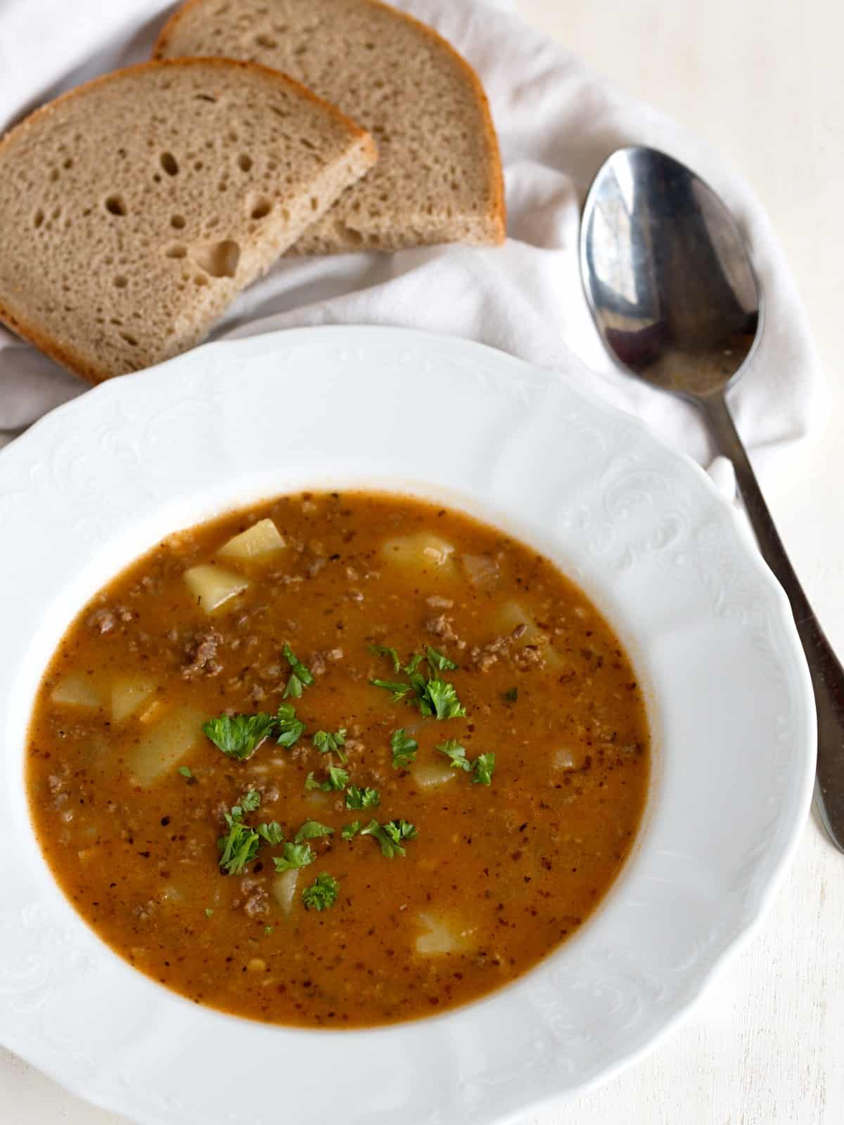 Czech goulash soup in a white plate, with slices of rye bread. 