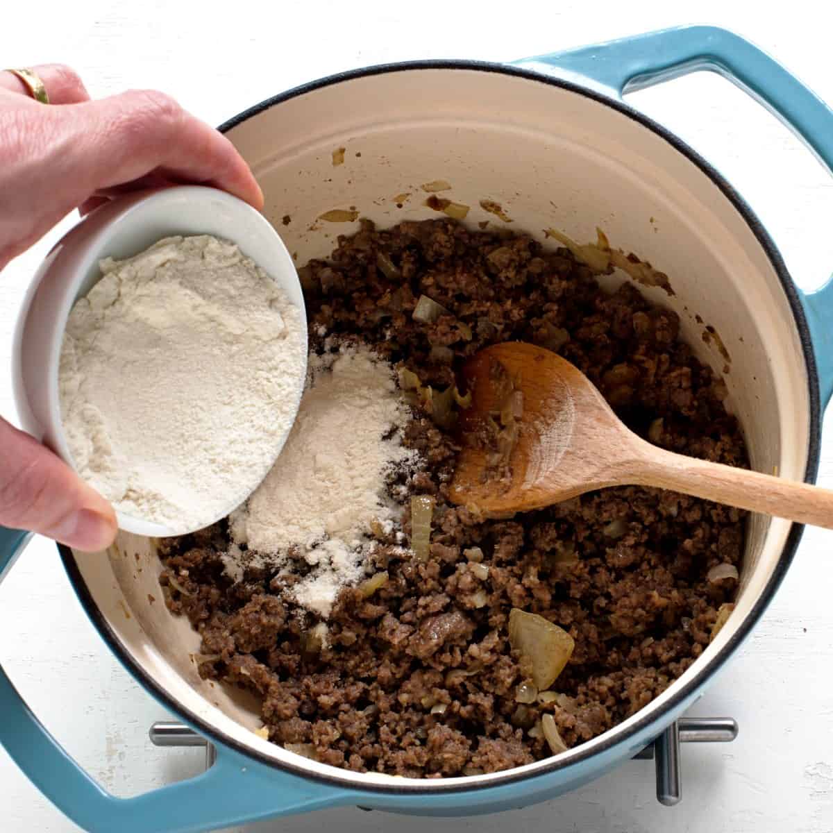 Adding flour to a pot with fried ground beef. 