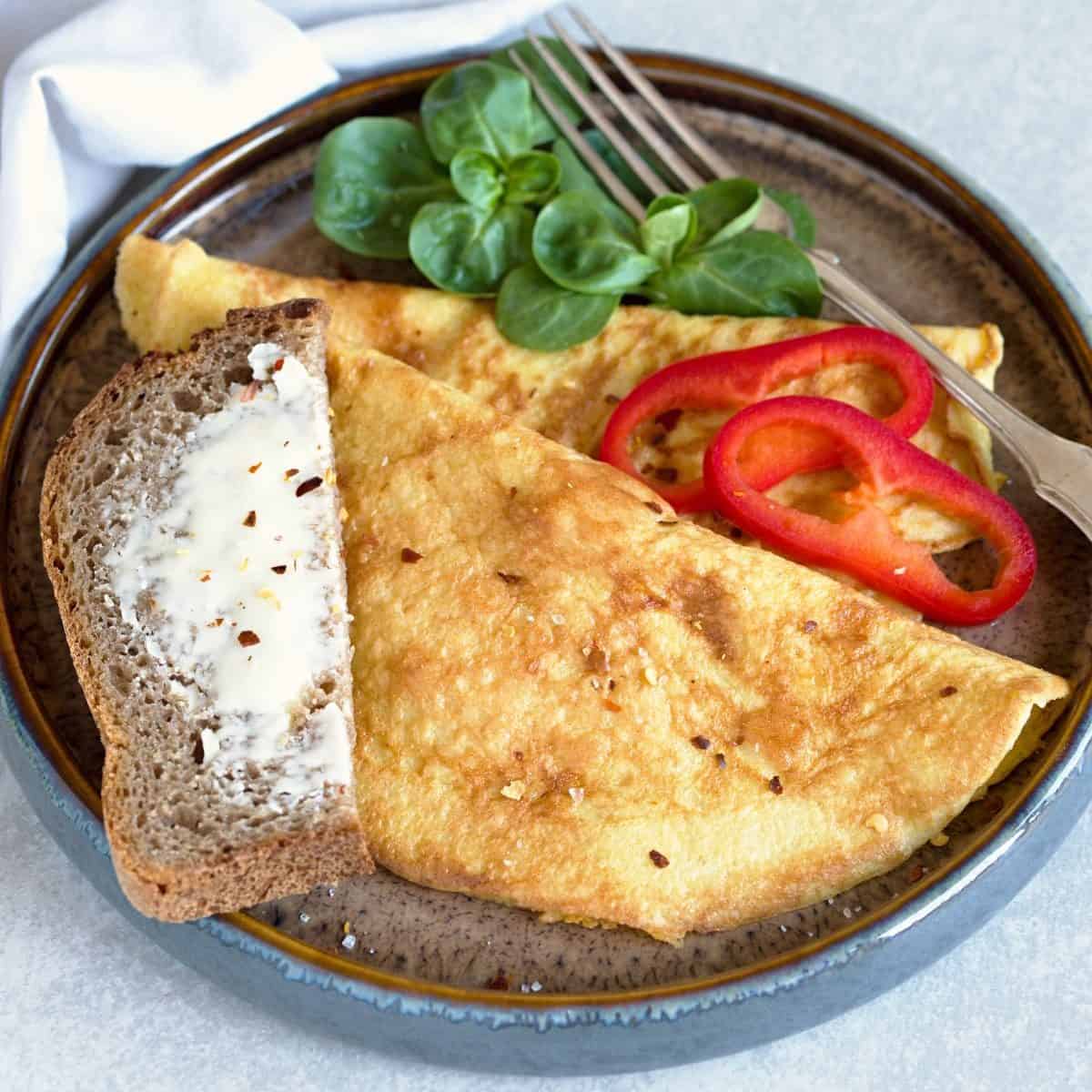 Fluffy omelette served with vegetables and buttery bread.