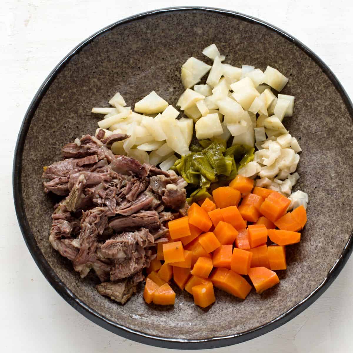 Vegetables cut in cubes, cooked beef on a brown plate.