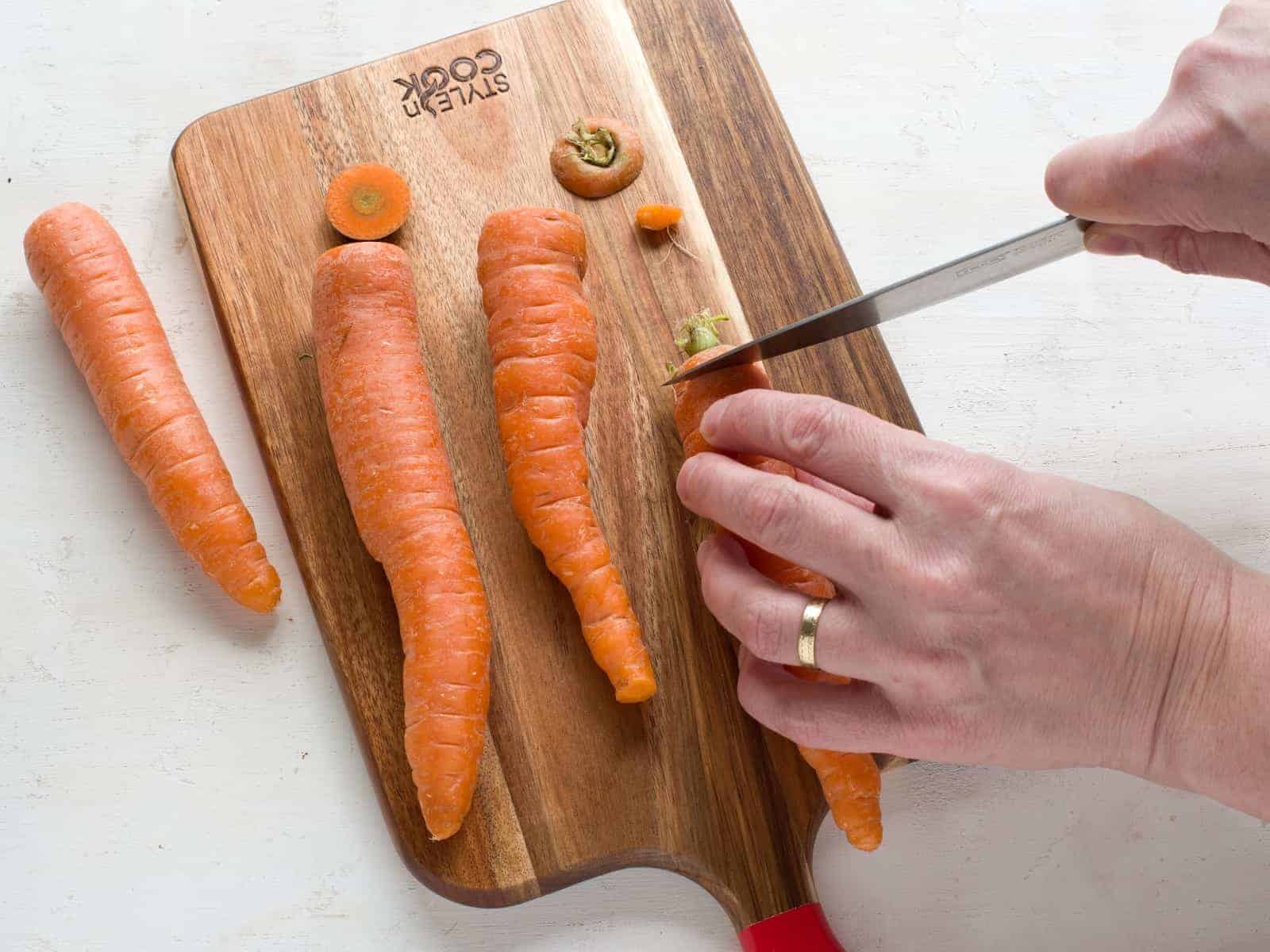 Cutting the ends of a carrot on a cutting board.
