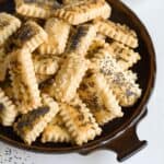 Small biscuits topped with poppyseed and caraway arranged on a brown plate.