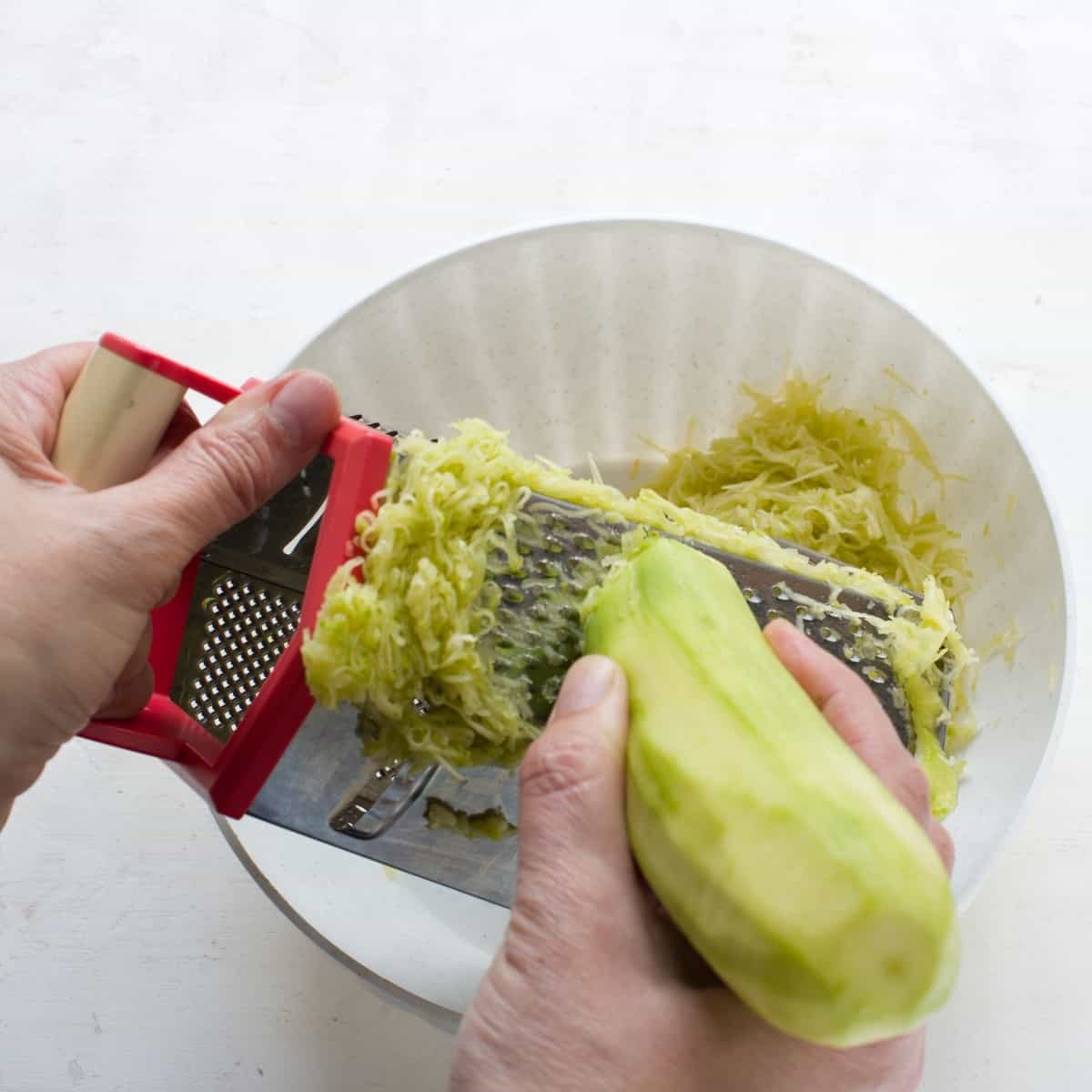 Shredding peeled zucchini on a hand grater box.