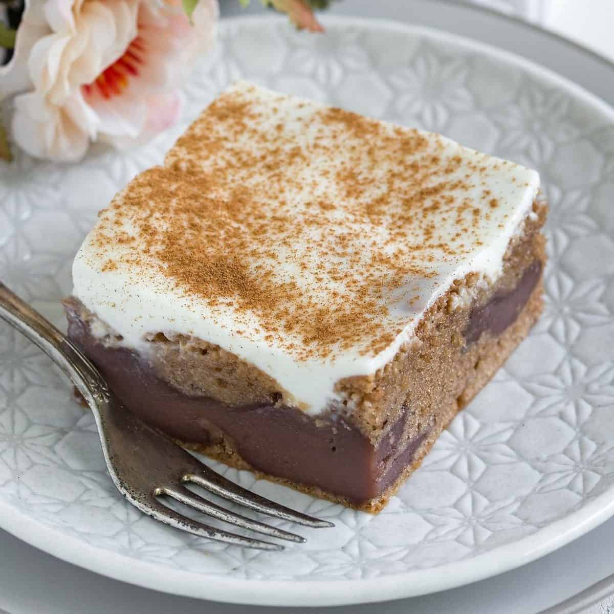 Sliced chocolate coffee cake with sour cream topping, served on a white plate.