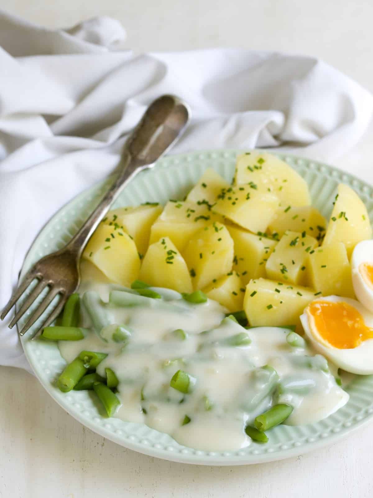 Green beans with white sauce served with boiled potatoes and hard-boiled egg.