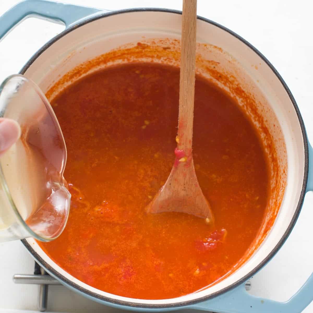 Making tomato soup with broth, in a blue pot.