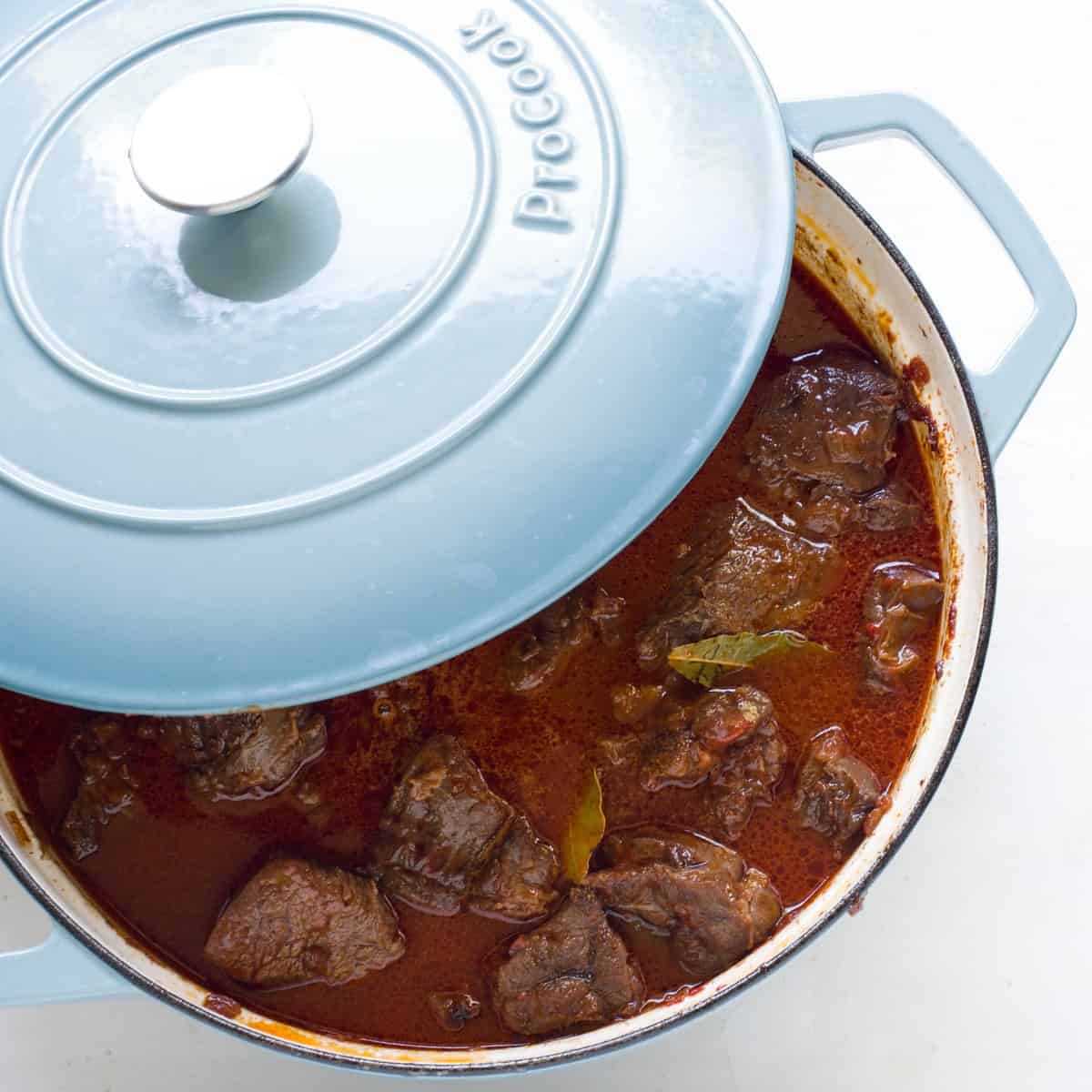 Braising goulash in a pot with a blue lid.
