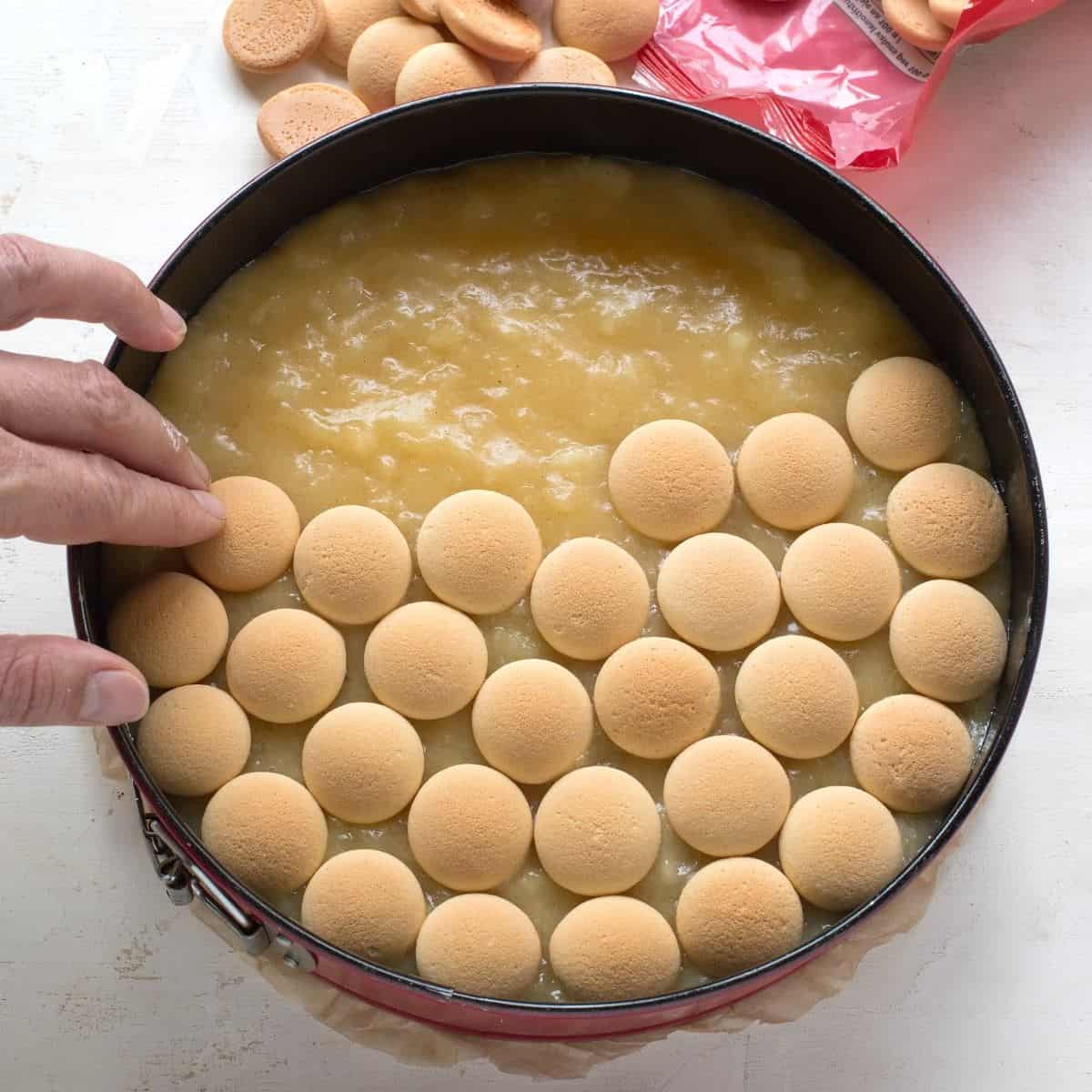 Placing biscuits on apple jelly, making aplle cake.