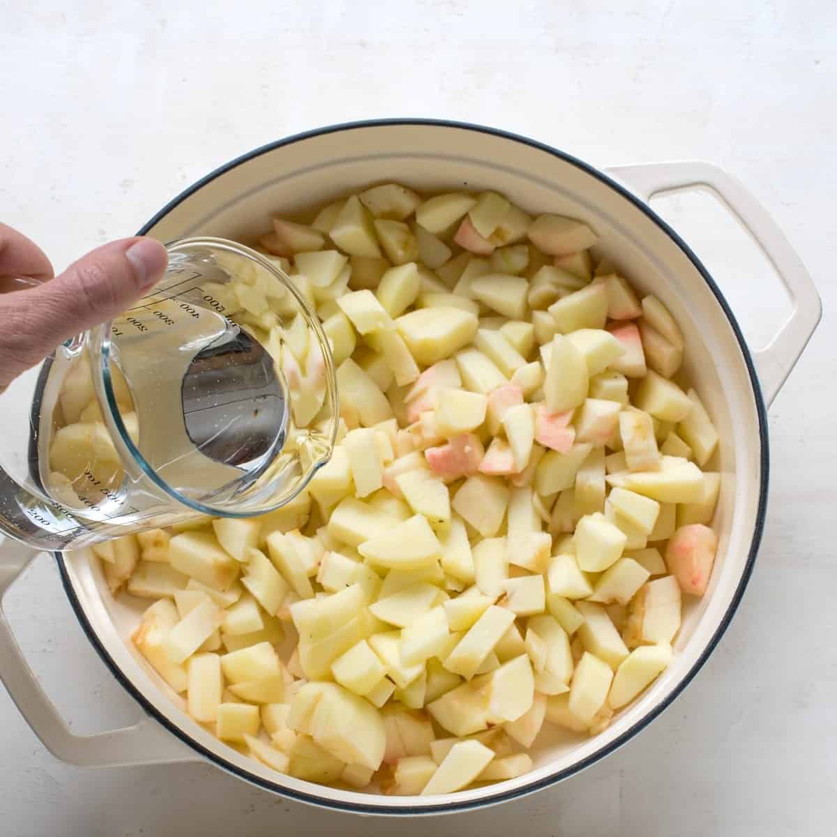 Pouring water over sliced apples placed in a pan.