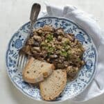 Fresh mushrooms with scrambled eggs served on a blue white plate, with two slices of rye bread.