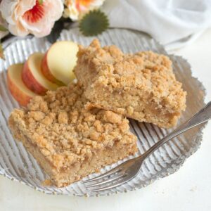 Sliced crumb cake with shredded apples, served on a plate with a fork.