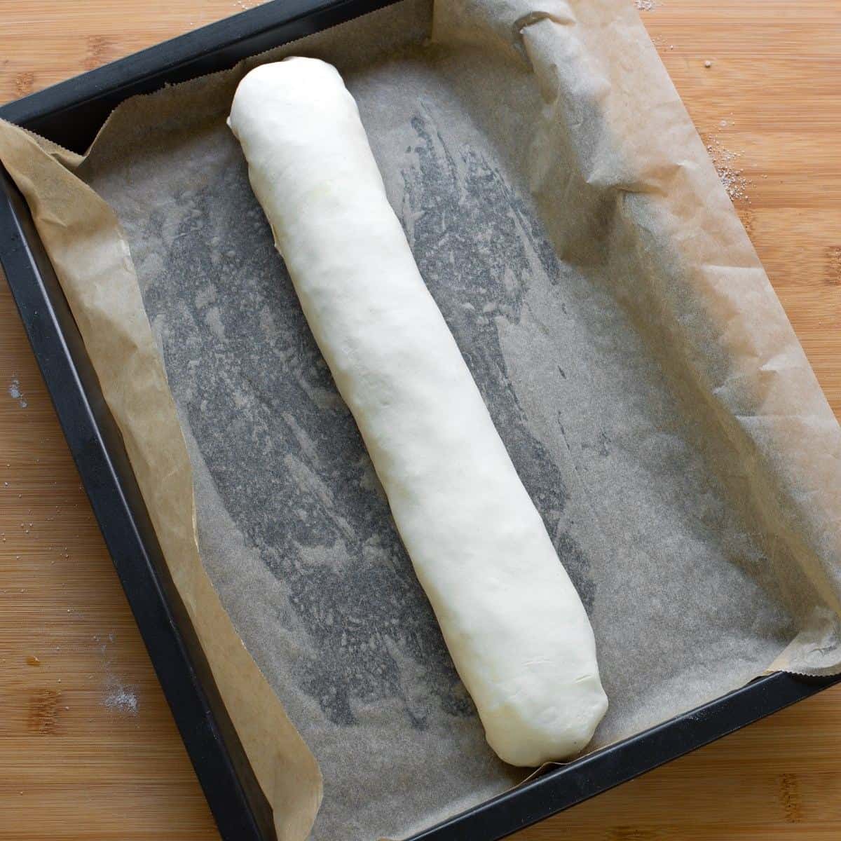 Rolled apple strudel on baking sheet, lined with parchment paper.