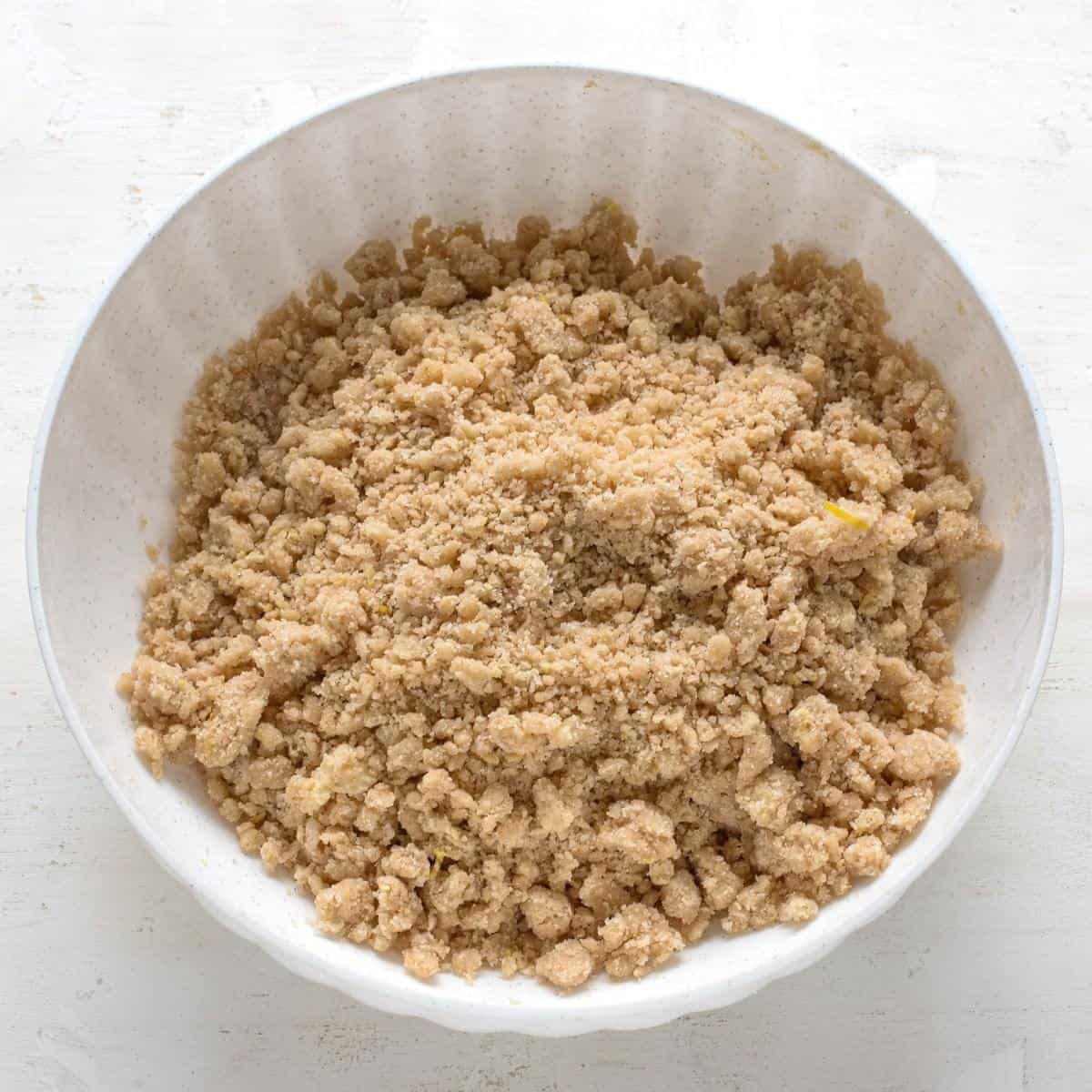 Soft crumbs for making apple crumb cake, in a white mixing bowl.