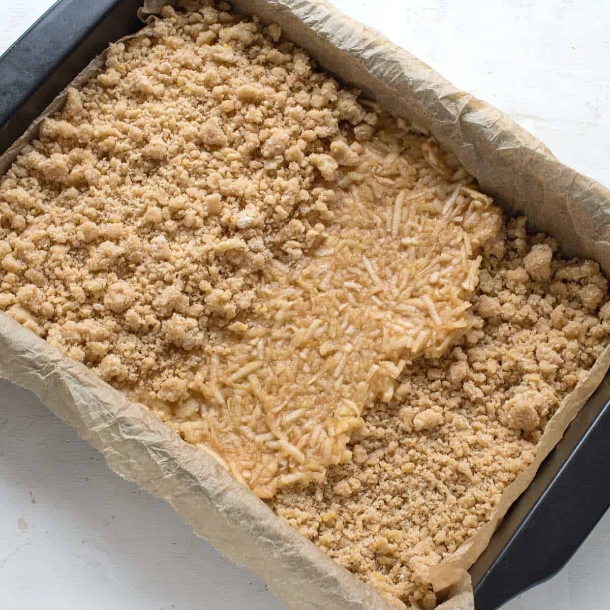 Process photo of making an apple cinnamon crumb cake. There are seen all three layers in the baking pan while completing the cake.