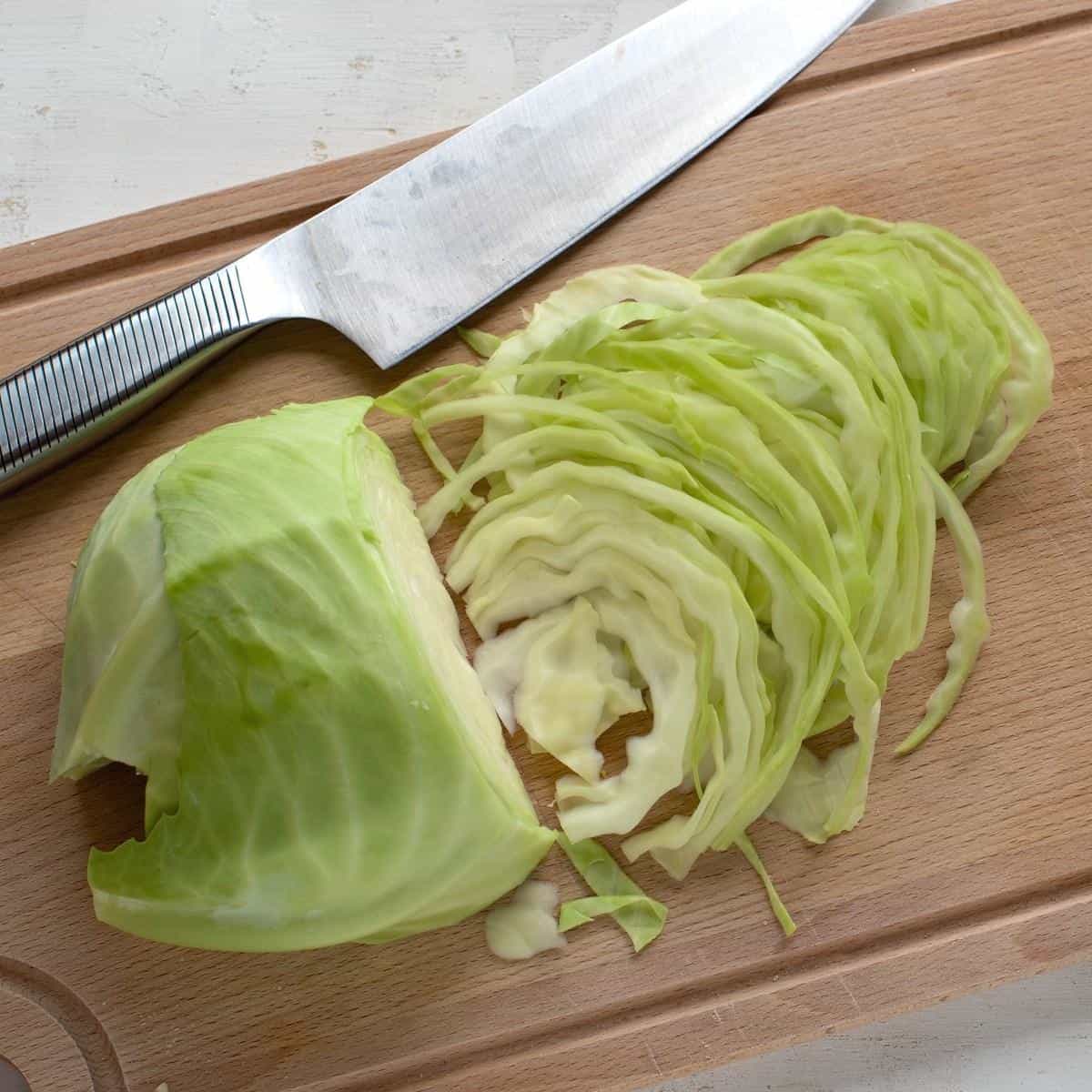 Slicing green cabbage on a cutting board with a knife.