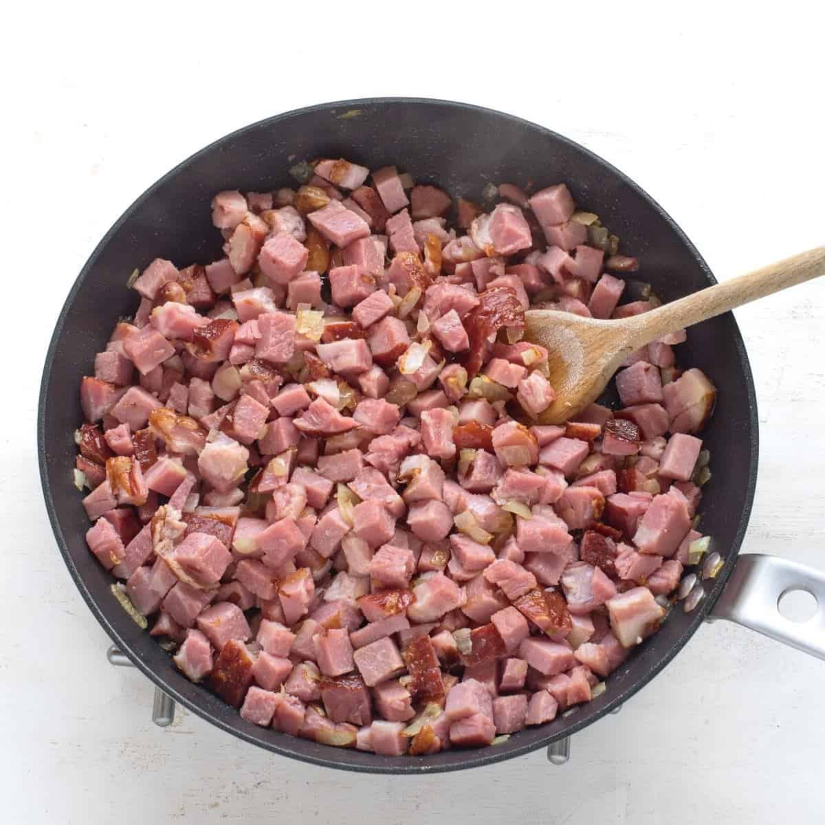 Diced smoked meat frying in a pan with chopped oinon.