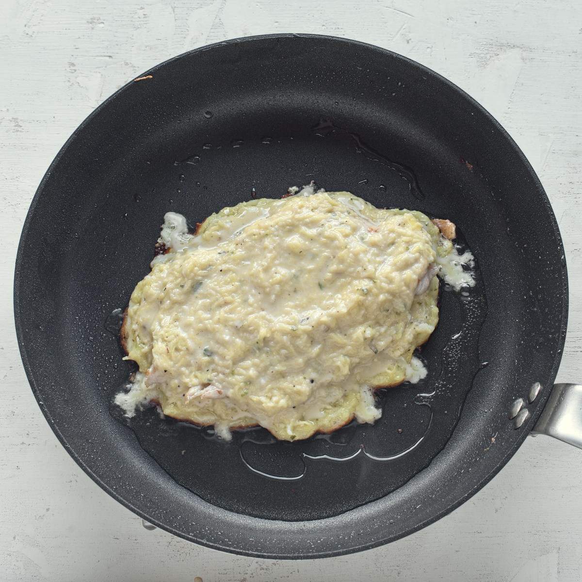 Potato pancake with chicken breast steak is frying in a pan.