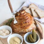 Roasted pork knuckle served on a wooden plate with horseradish, mustard and dill pickles.