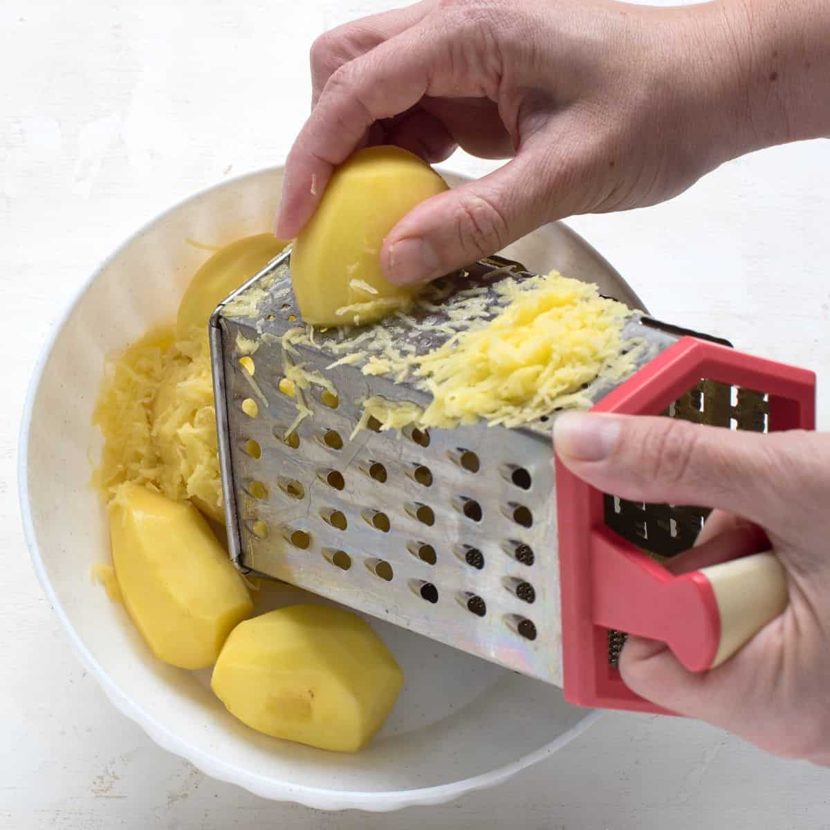 Shredding potato by hand on a hand grater box.