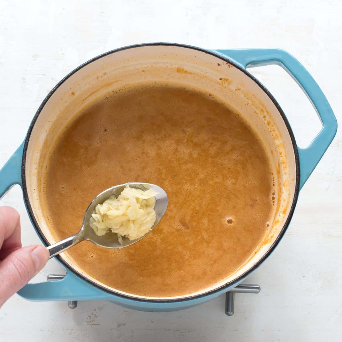 Adding crushed garlic to a blue pot of tripe soup.
