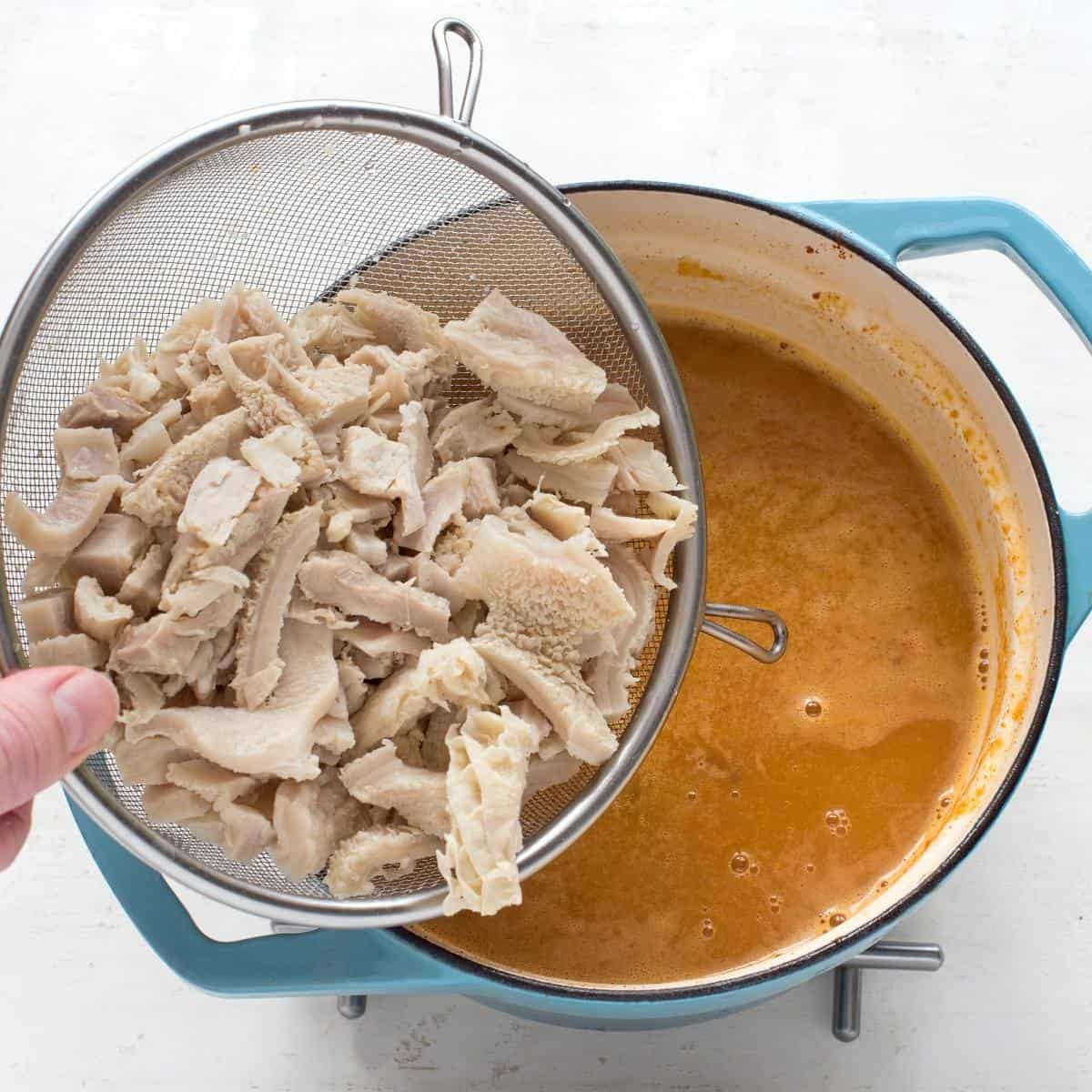 Adding strips of tripe to a blue pot of soup.