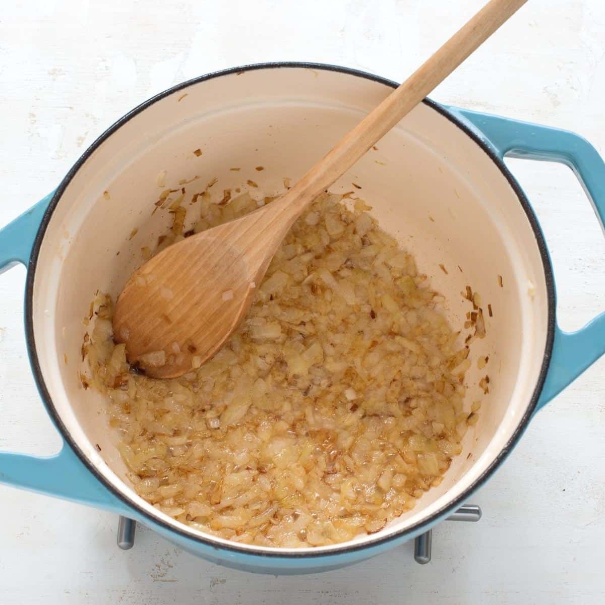 Frying onions in a blue pot with a wooden spoon.