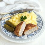 Ground pork cheese schnitzel halved, served with a mashed potatoes on a white blue plate.
