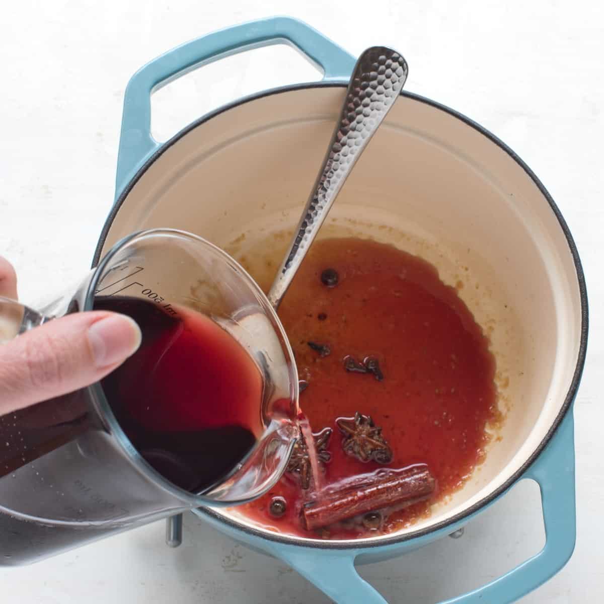 Making spiced wine - pouring red wine to a pot with spices.