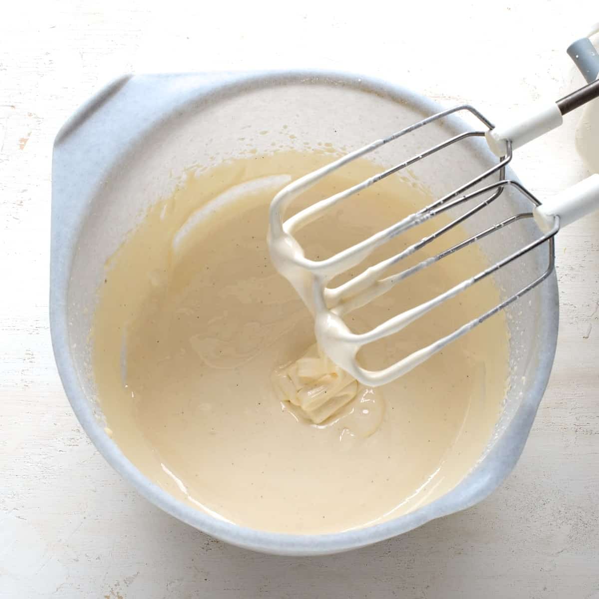 Whipped eggs with sugar in a light gray bowl, using a handheld electric mixer.