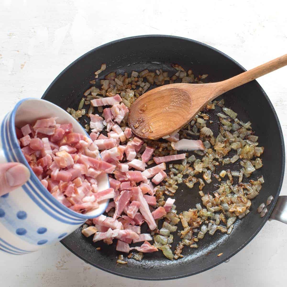 Frying onions in a pan, adding diced ham.