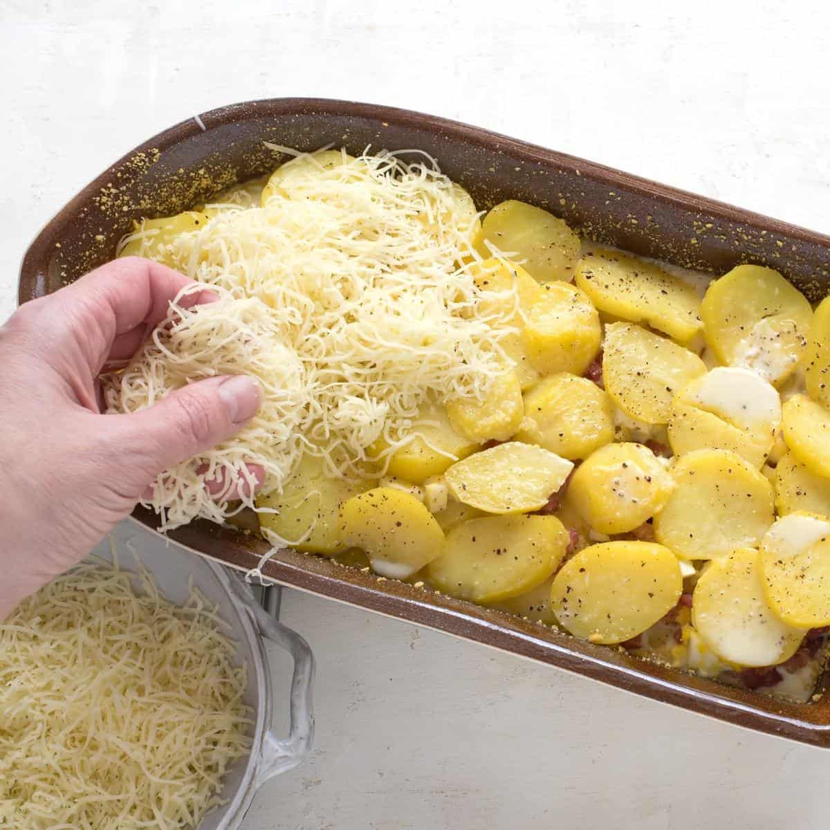 Sprinkling grated cheese over potato gratin.