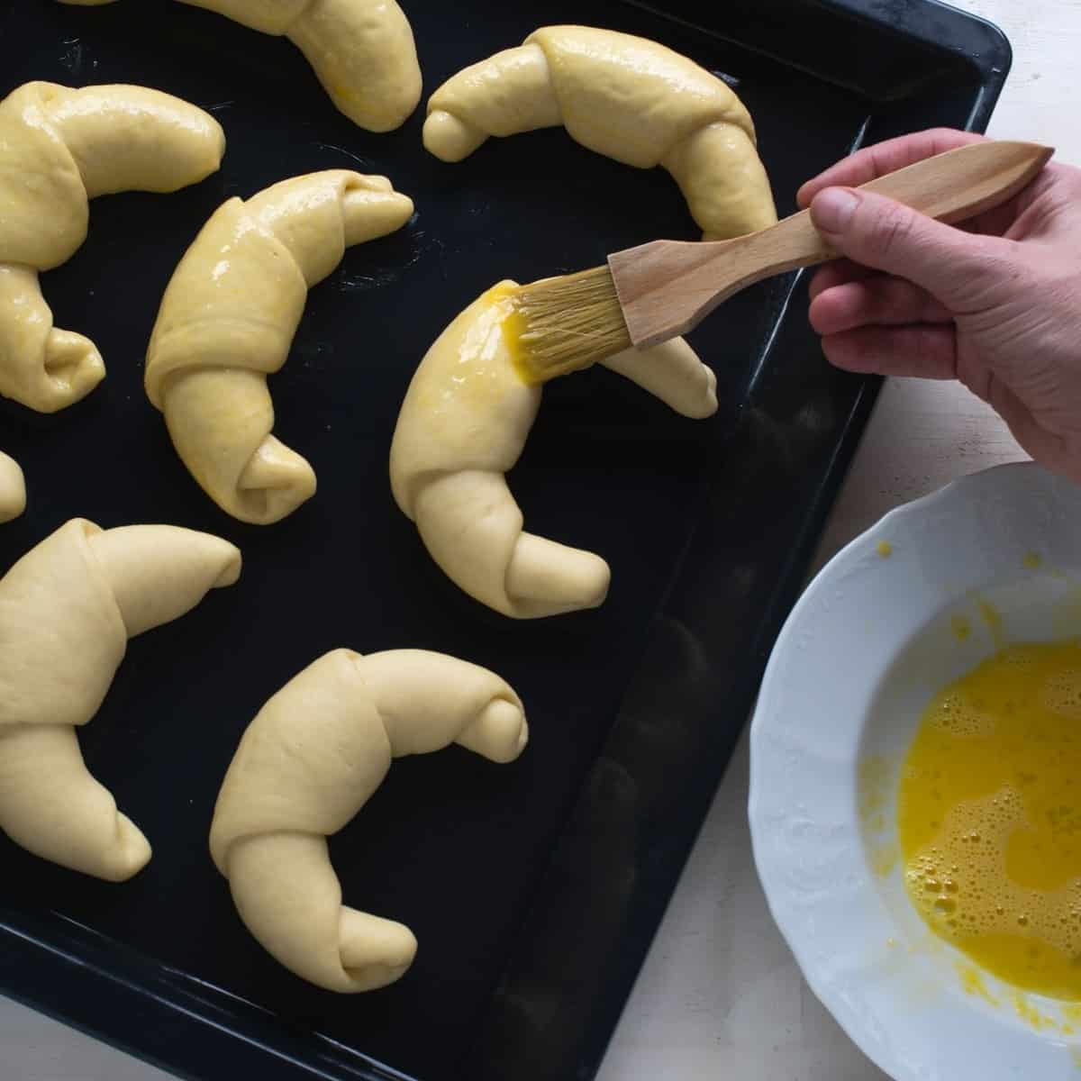 Brushing loupacky crescent rolls with egg wash.