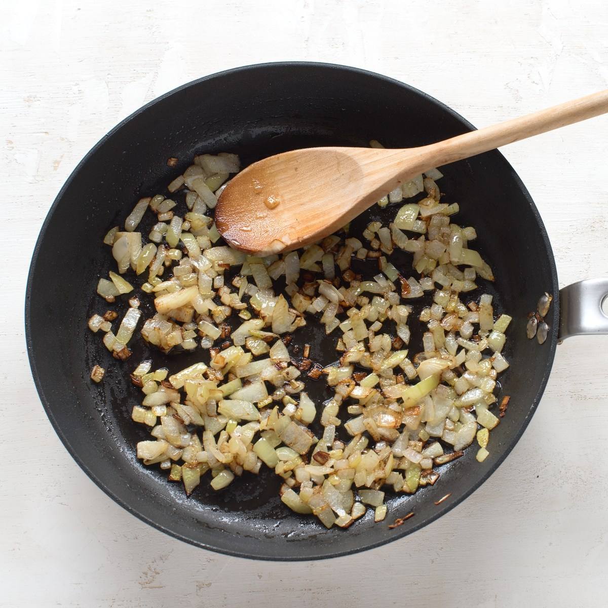 Sauteed onion in a black skillet, with a wooden spoon.