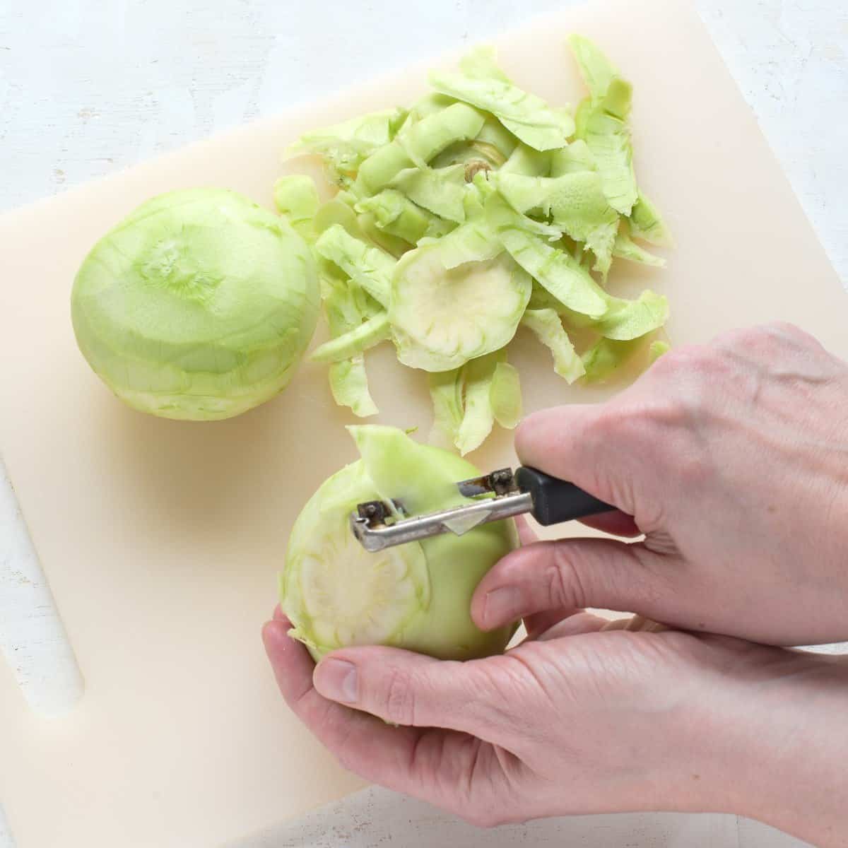 Peeling kohlrabi by hand with a vegetable peeler.