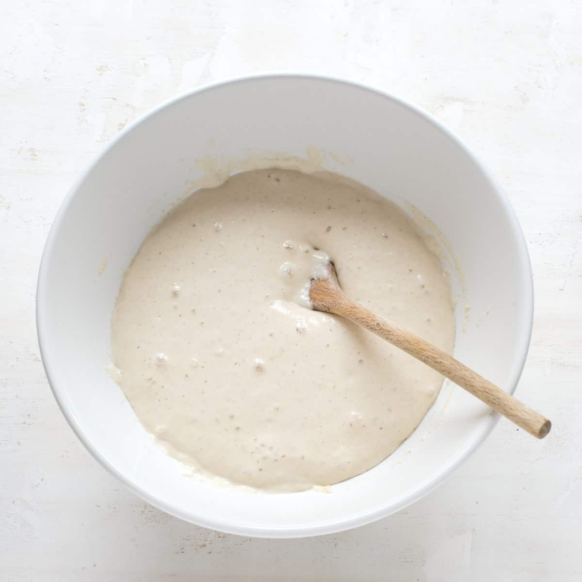 Yeast dough rising in a white bowl with a wooden spoon.