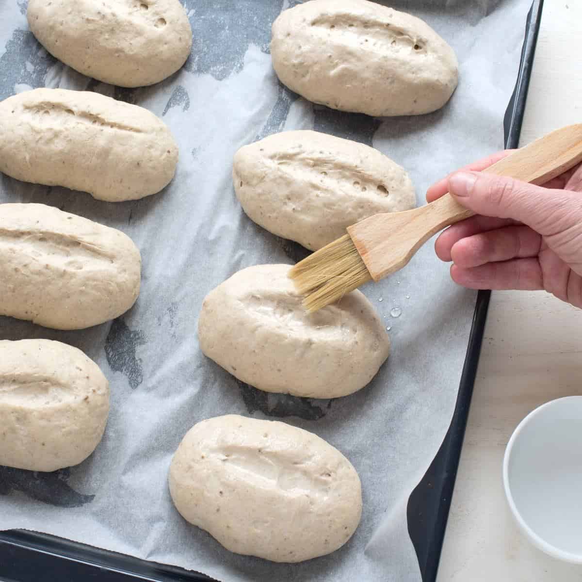 Brushing rye rolls placed on a baking sheet with water.