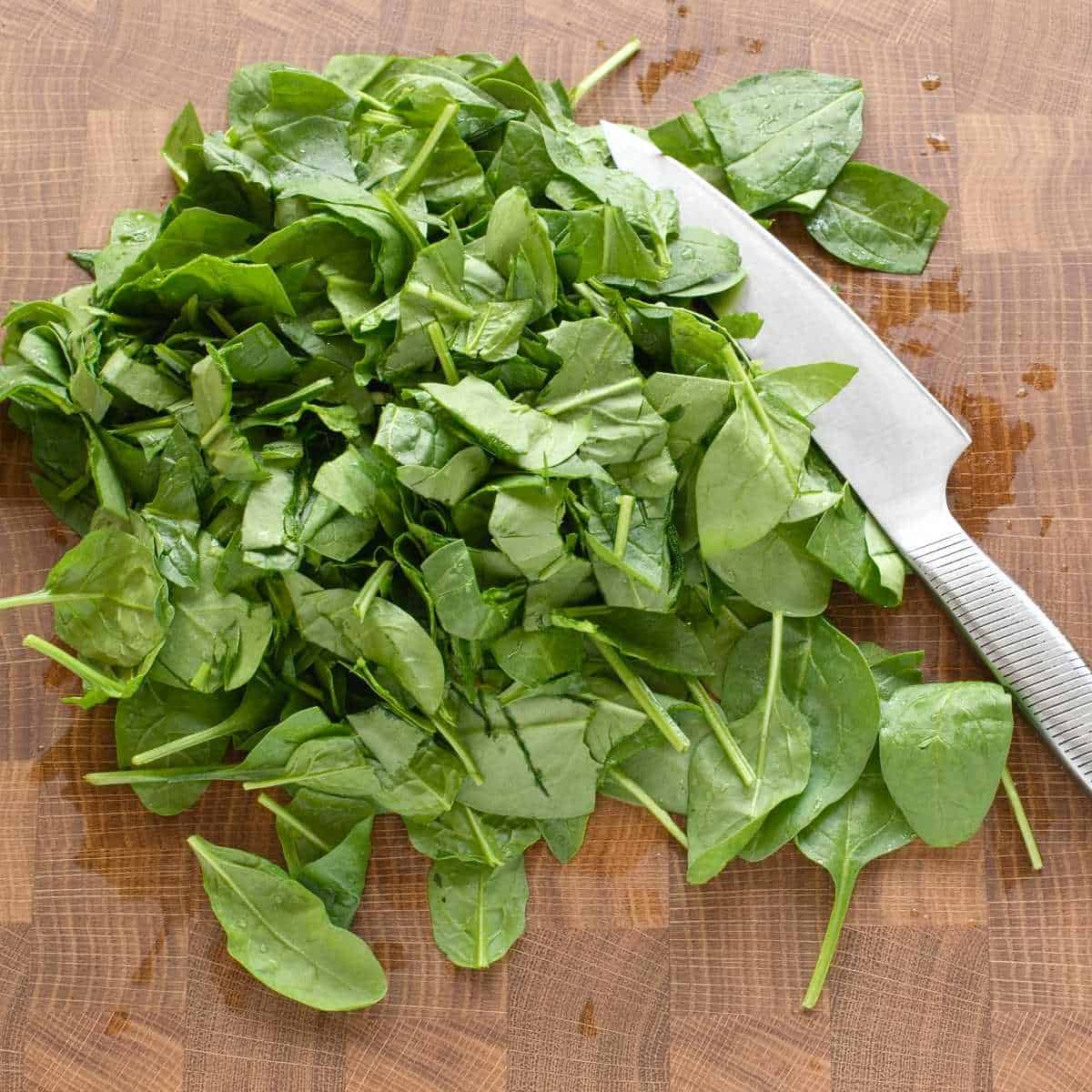 Chopping green baby spinach leaves with a knife, on wooden kitchen board.