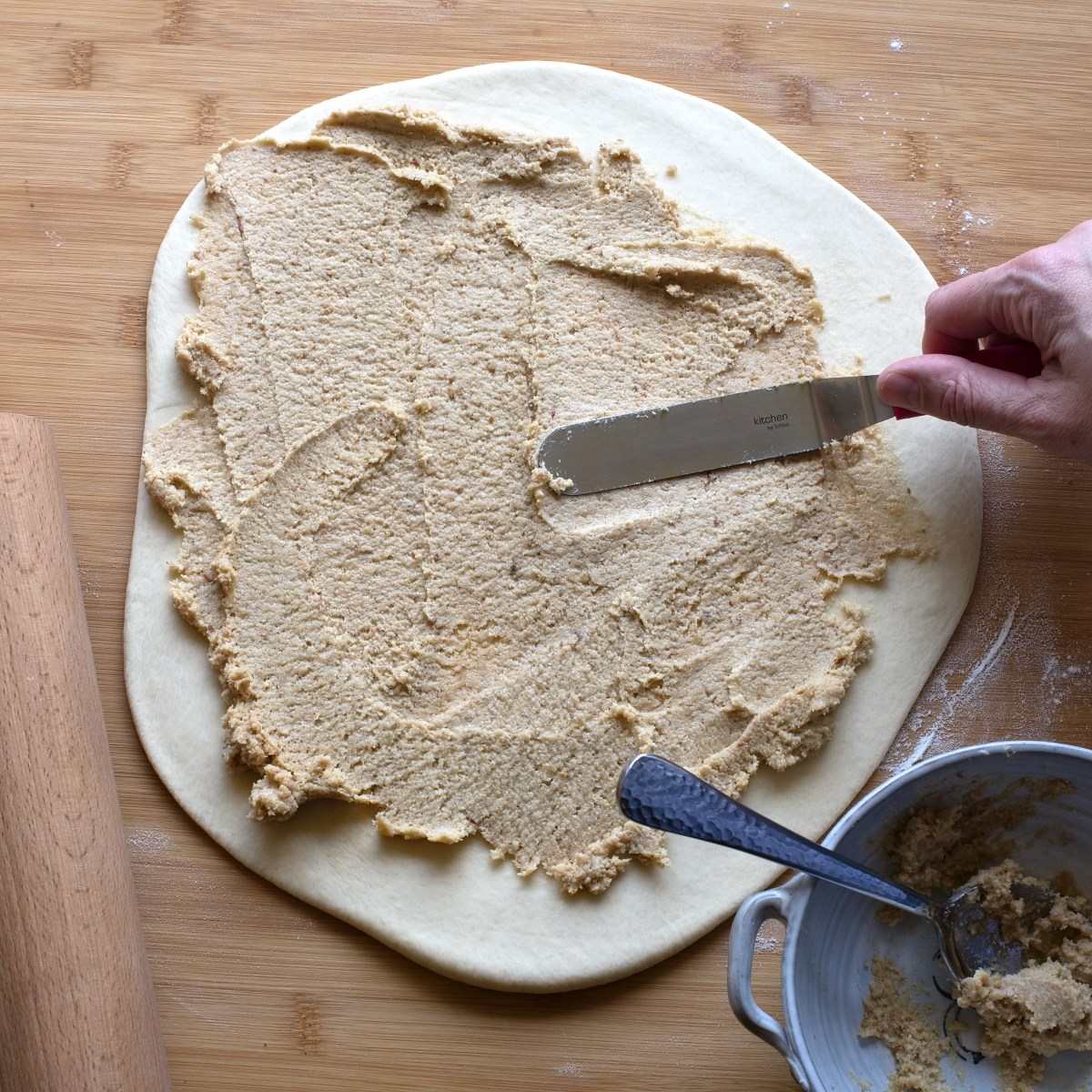 Brushing ground cracklings over rolled-out dough.