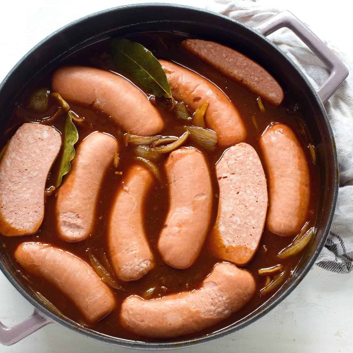 Halved sausages put in a pot with dark beer gravy.