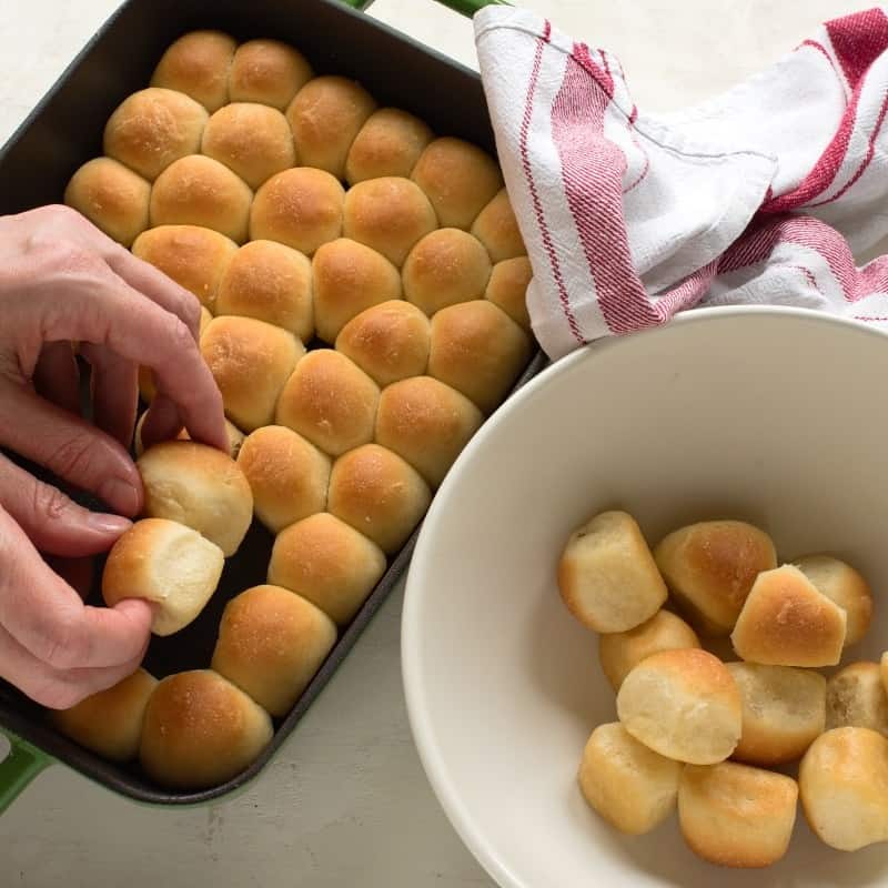 Transfering baked bobalki bread balls from baking dish to a white bowl.