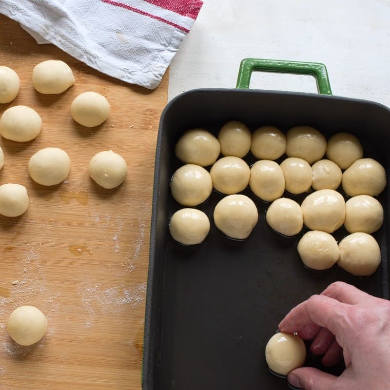 Putting raised balls into a baking dish, rolling them in oil.