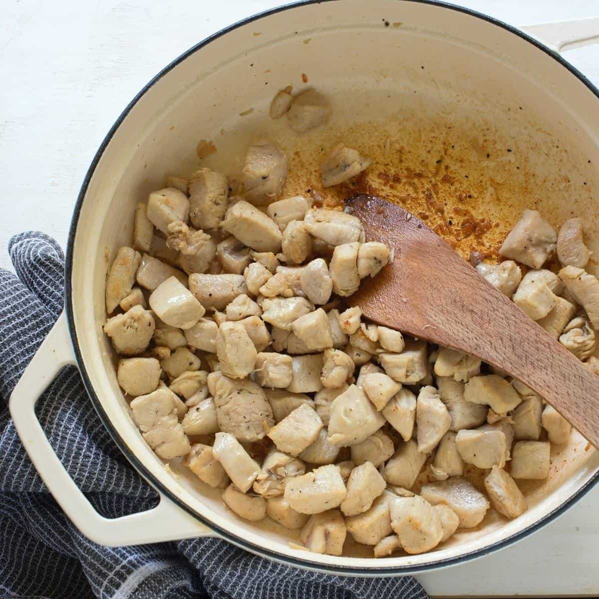 Frying chicken breast cubes in a pan.