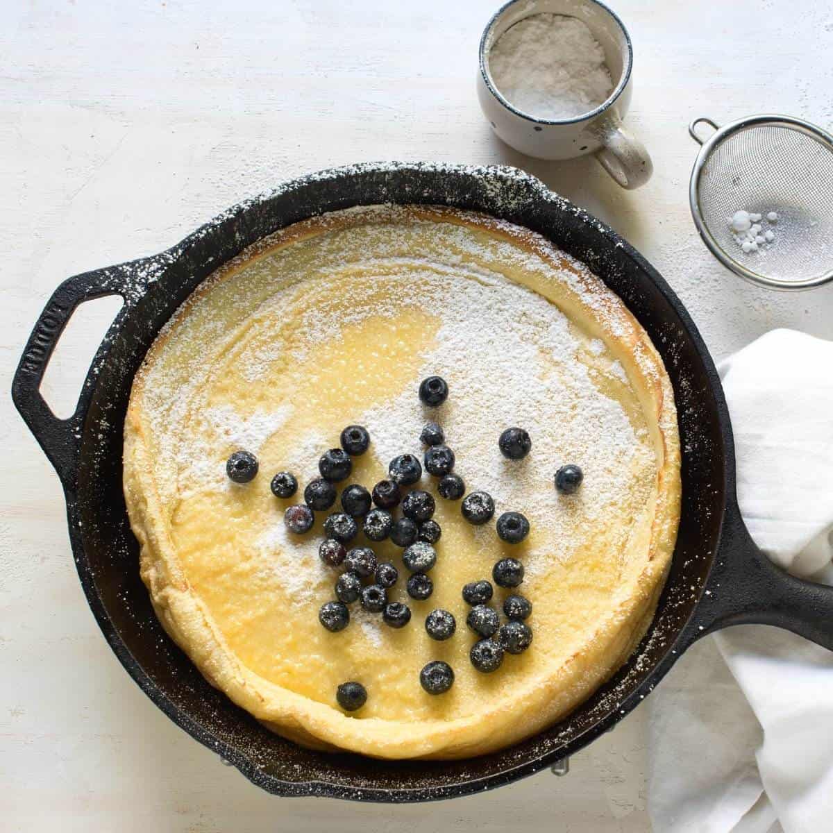 Puffed pancake in a skillet, sprinkled with powdered sugar, with blueberries.