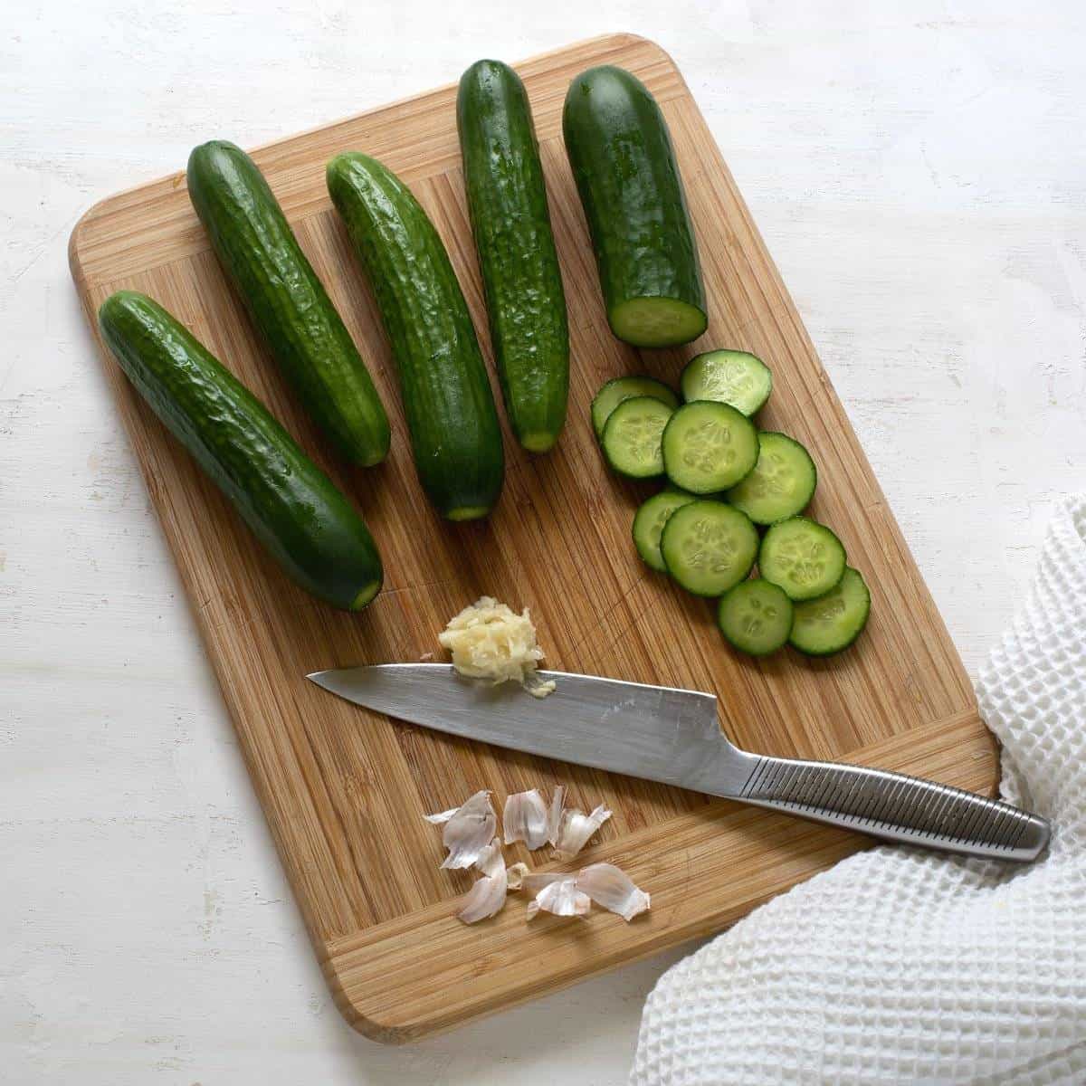 Slicing cucumbers and mashed garlic, on a kitchen wooden board, with a knife.