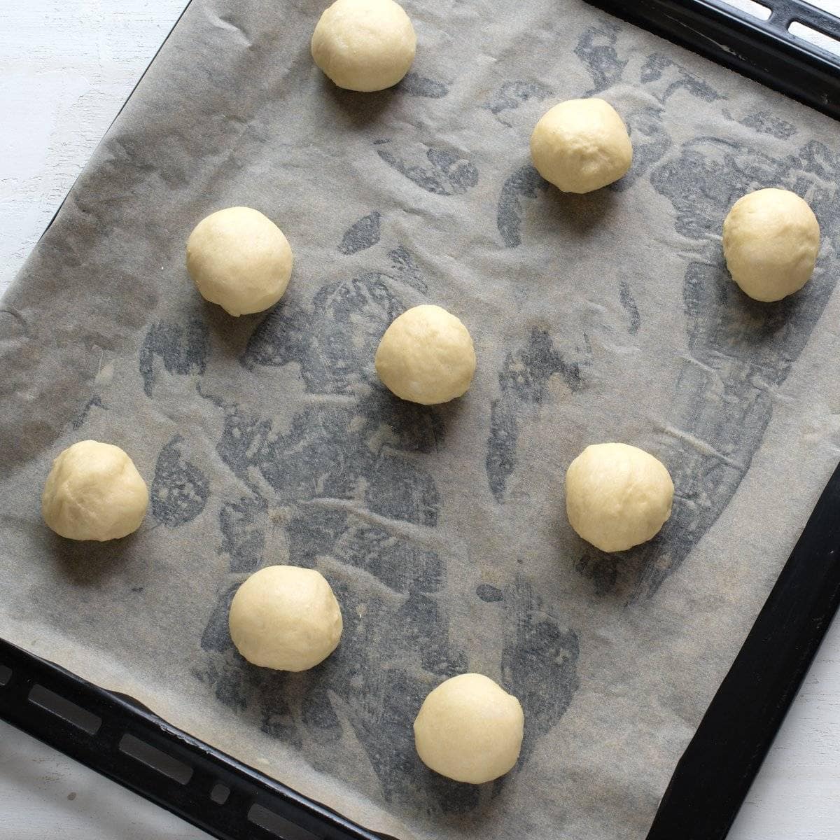Balls of yeast dough placed on a lined baking sheet.