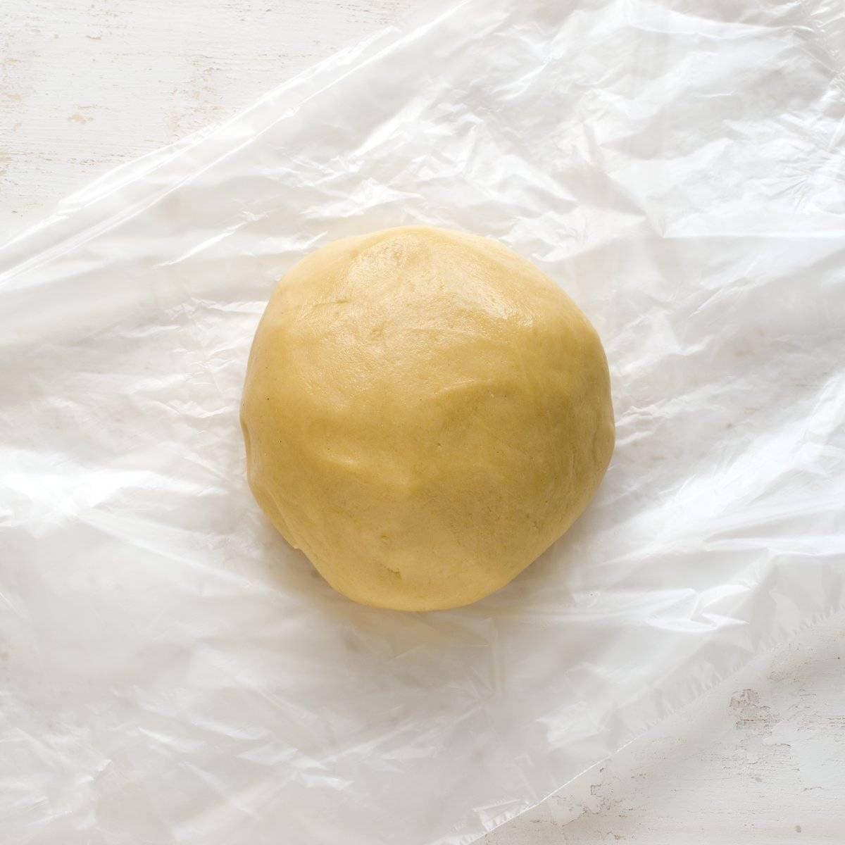 A ball of soft honey dough, placed on a plastic wrap.